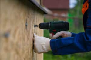 Person using power drill to board up window with plywood