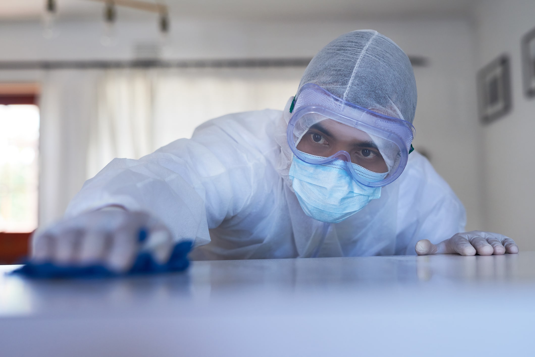 Man in a hazmat suit carefully cleaning a surface in a house after a death